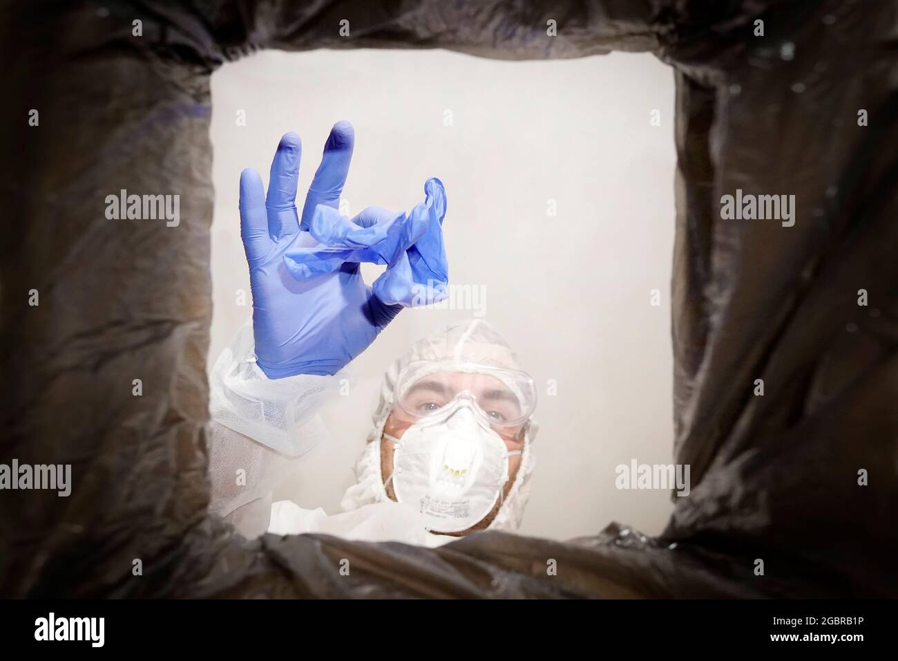 un homme en costume de protection jette un gant médical usagé dans une poubelle. Vue de dessous de la corbeille. Le problème du recyclage et de la pollution de la p Banque D'Images