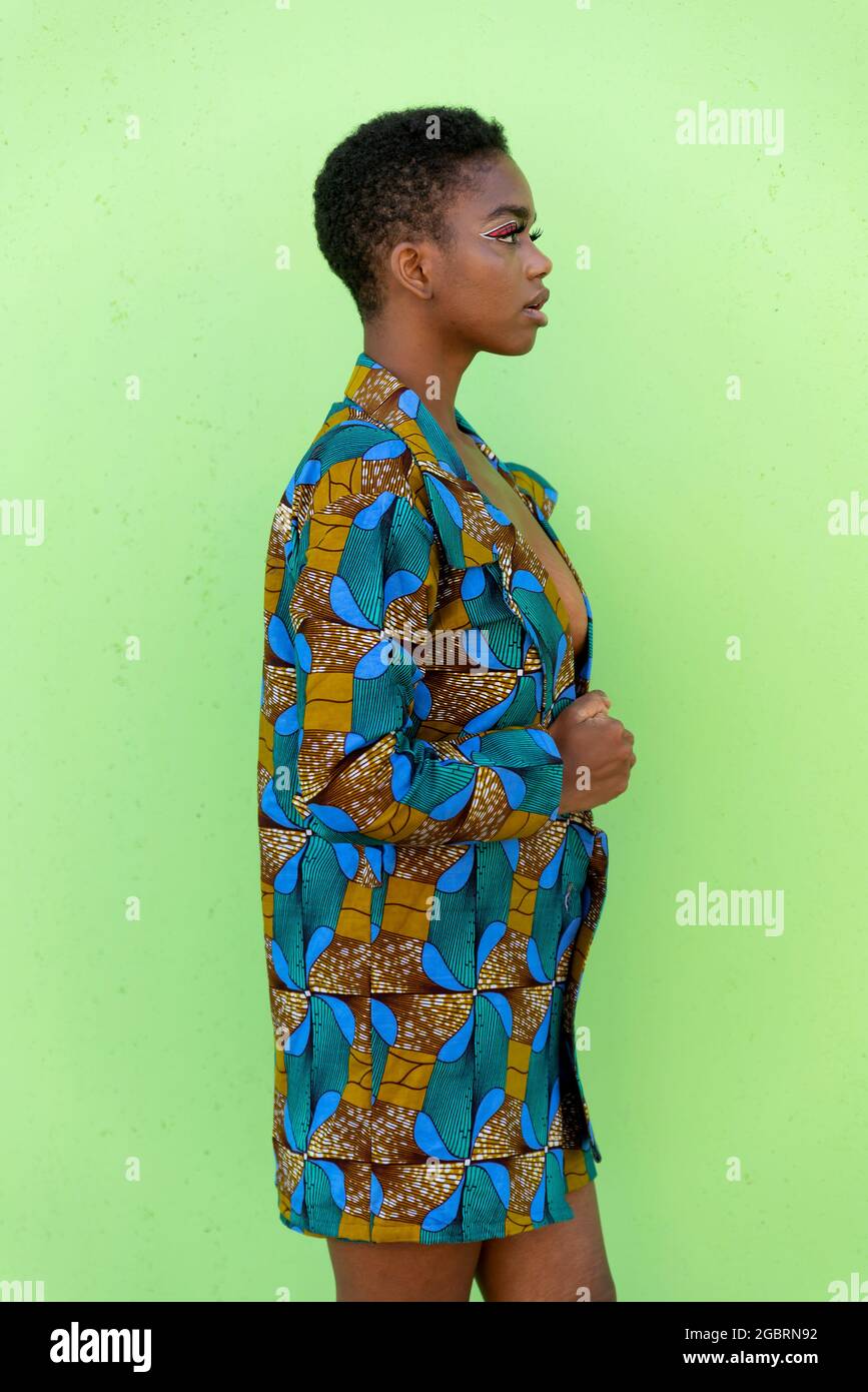 Jeune femme noire en tissu africain traditionnel, regardant loin sur fond de pistache Banque D'Images