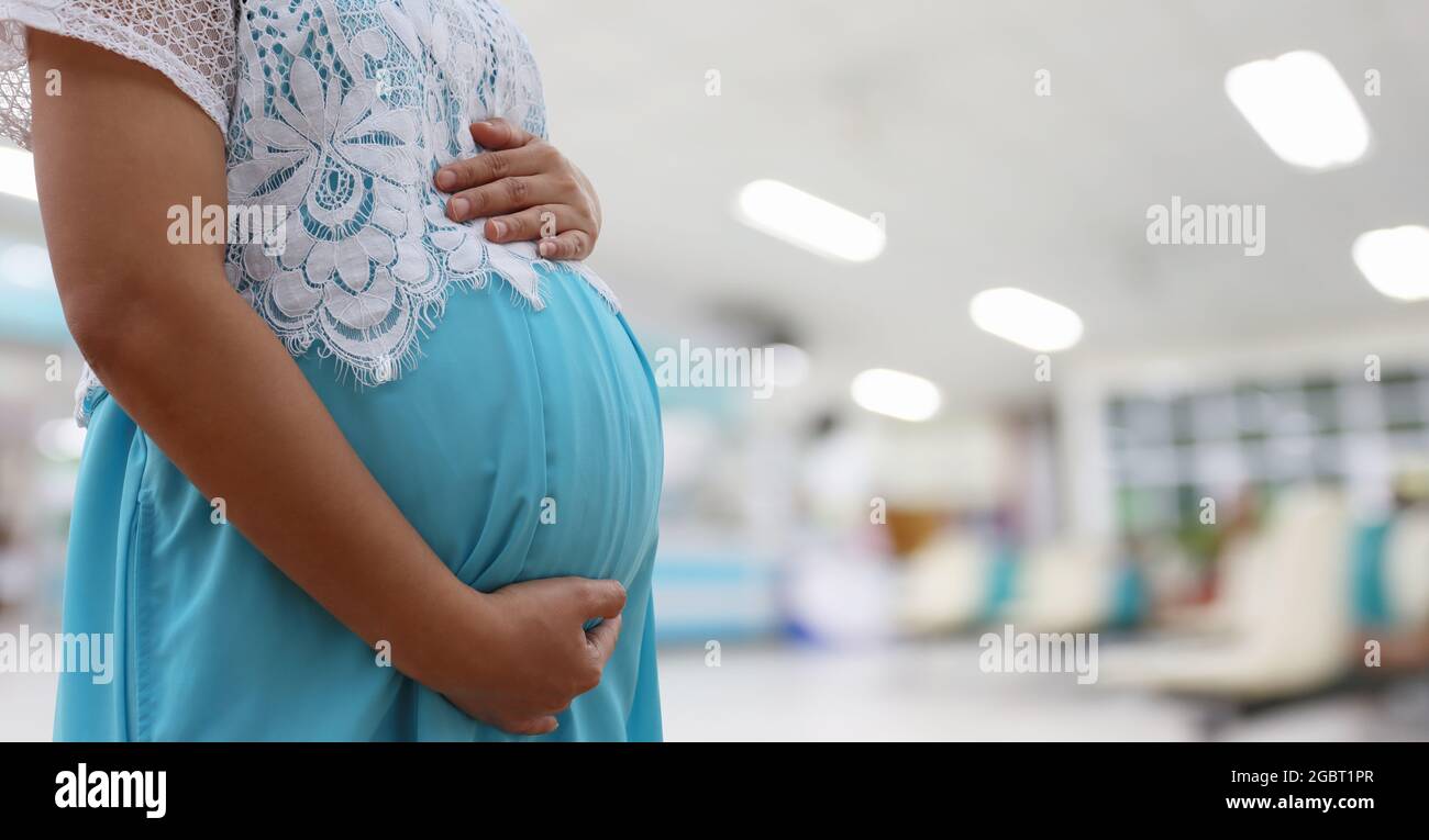 Femme enceinte vêtue d'une robe bleue sur un fond flou de l'hôpital et avoir un espace de copie. Banque D'Images