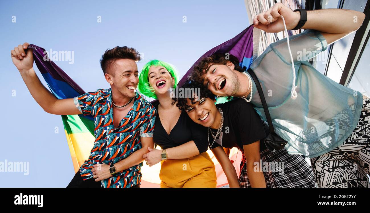 Groupe de jeunes LGBTQ célébrant la fierté ensemble en plein air. Groupe de reines souriant gaiement tout en tenant le drapeau de fierté arc-en-ciel. Quatre f Banque D'Images