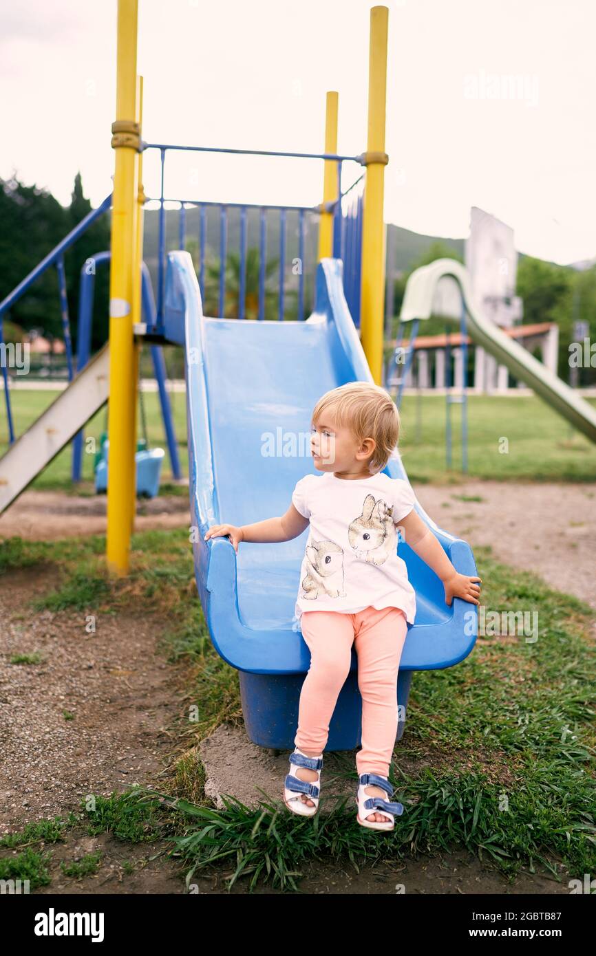 Une petite fille s'assoit sur un toboggan dans l'aire de jeux, tournant sa  tête Photo Stock - Alamy