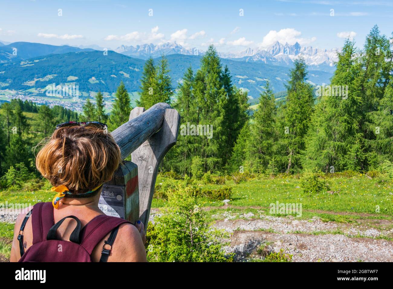 Un touriste sur un sentier de montagne, regardant à travers un télescope en bois le Hoher Dachstein et le massif Dachstein. Sommets de montagnes couverts de nuages. Haut Banque D'Images