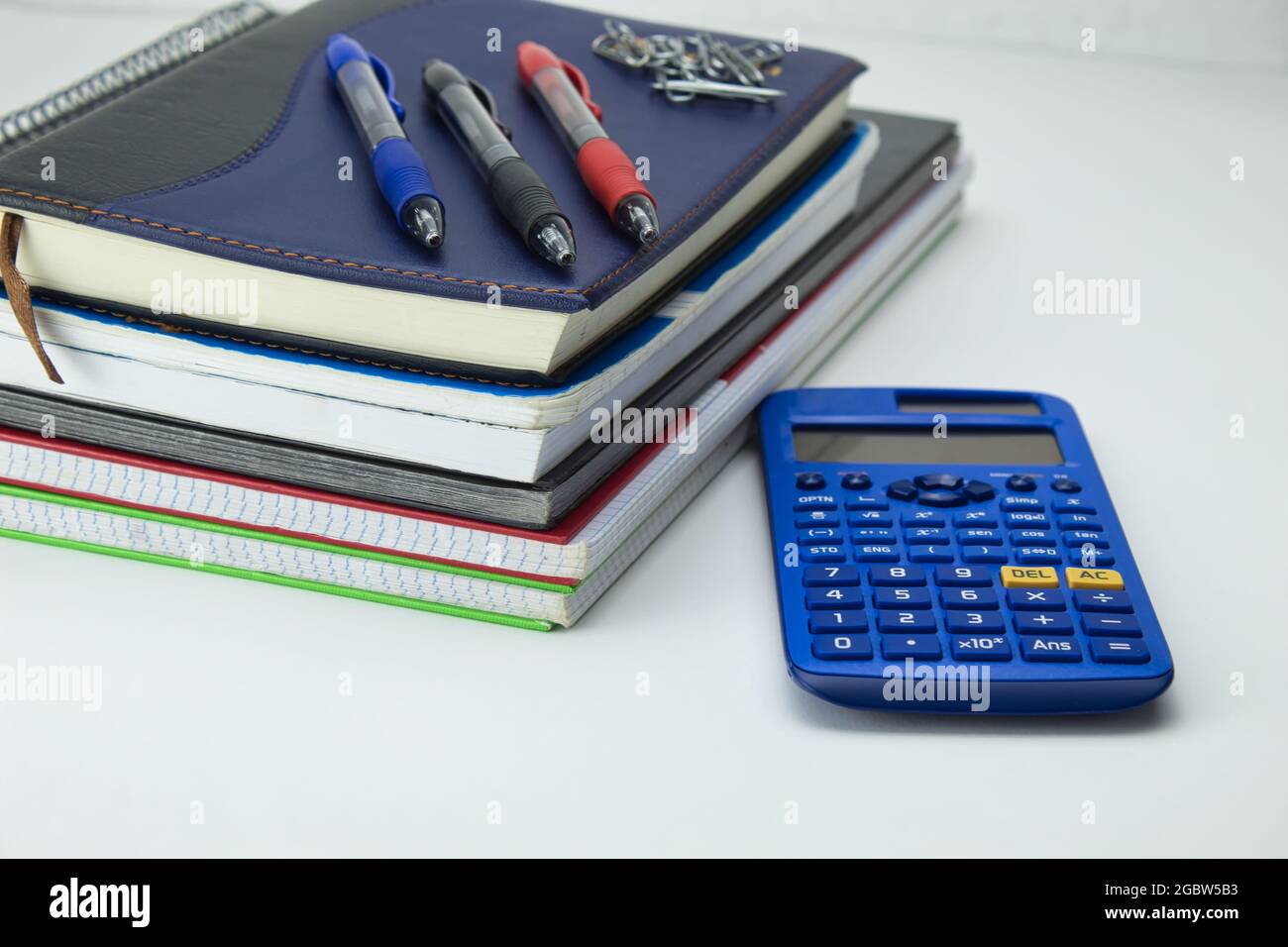 ensemble d'outils scolaires prêt pour la rentrée avec bloc-notes, stylos, marqueurs, trombones et calculatrice sur fond blanc Banque D'Images