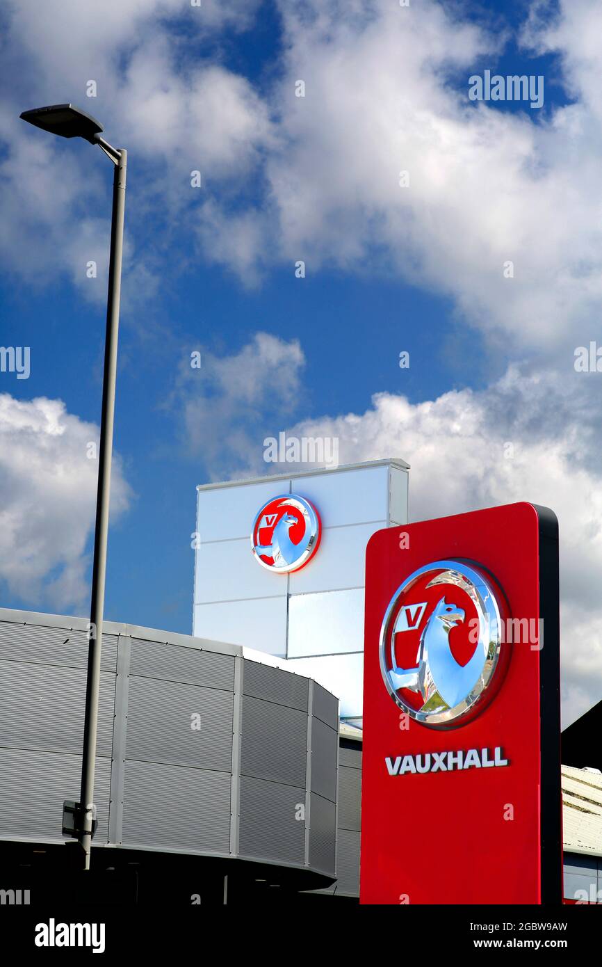 Le logo griffin de Vauxhall dans un concessionnaire automobile vu sur fond de ciel bleu et de nuages. Banque D'Images