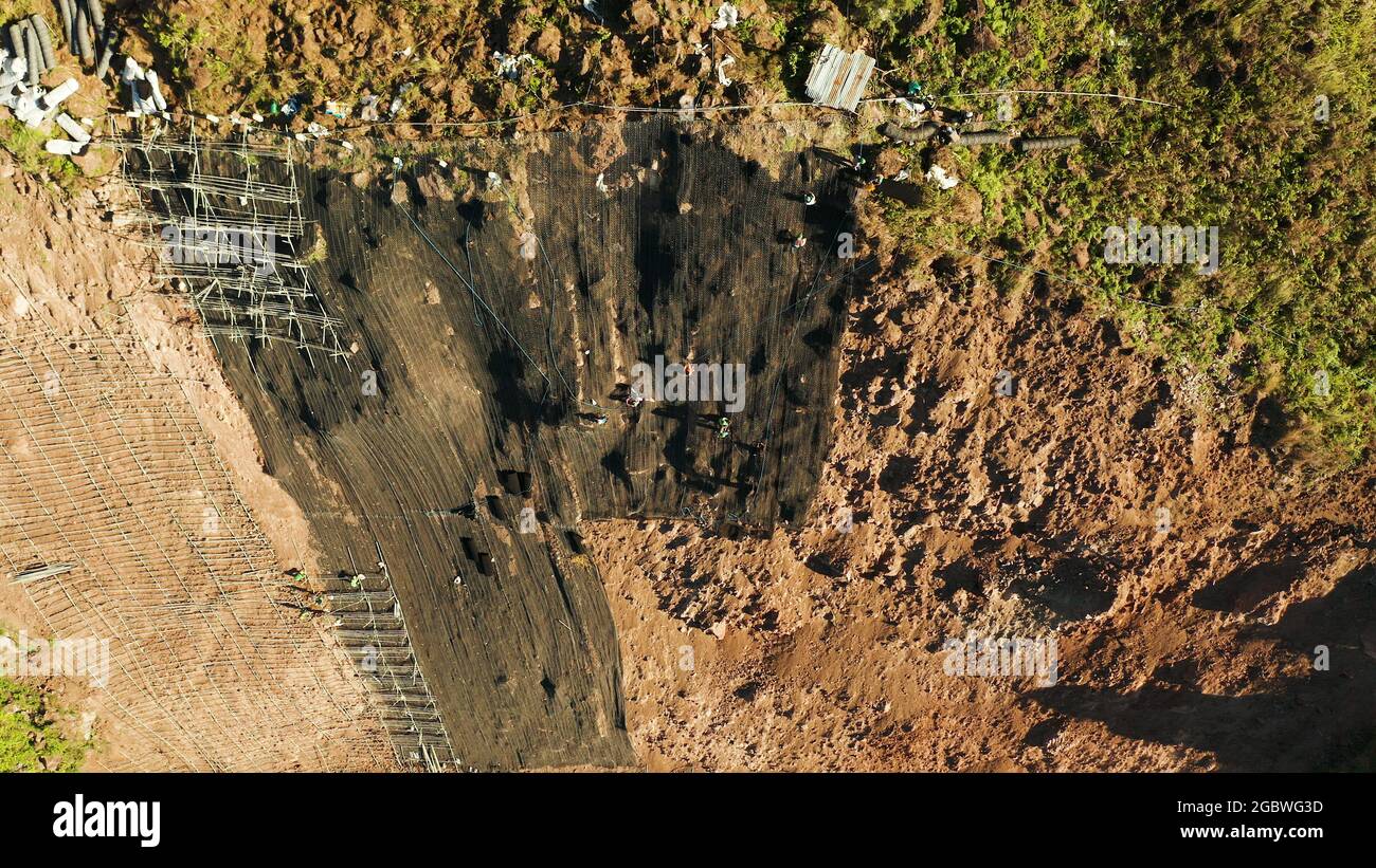 Renforcer les travailleurs la pente de la montagne avec le grillage de métal prévenir les chutes de pierres et glissements de terrain sur la route, vue ci-dessus. Les travailleurs de la construction de mur de béton anti-glissement prévenir protéger contre les glissements rocheux concept de sécurité. Banque D'Images