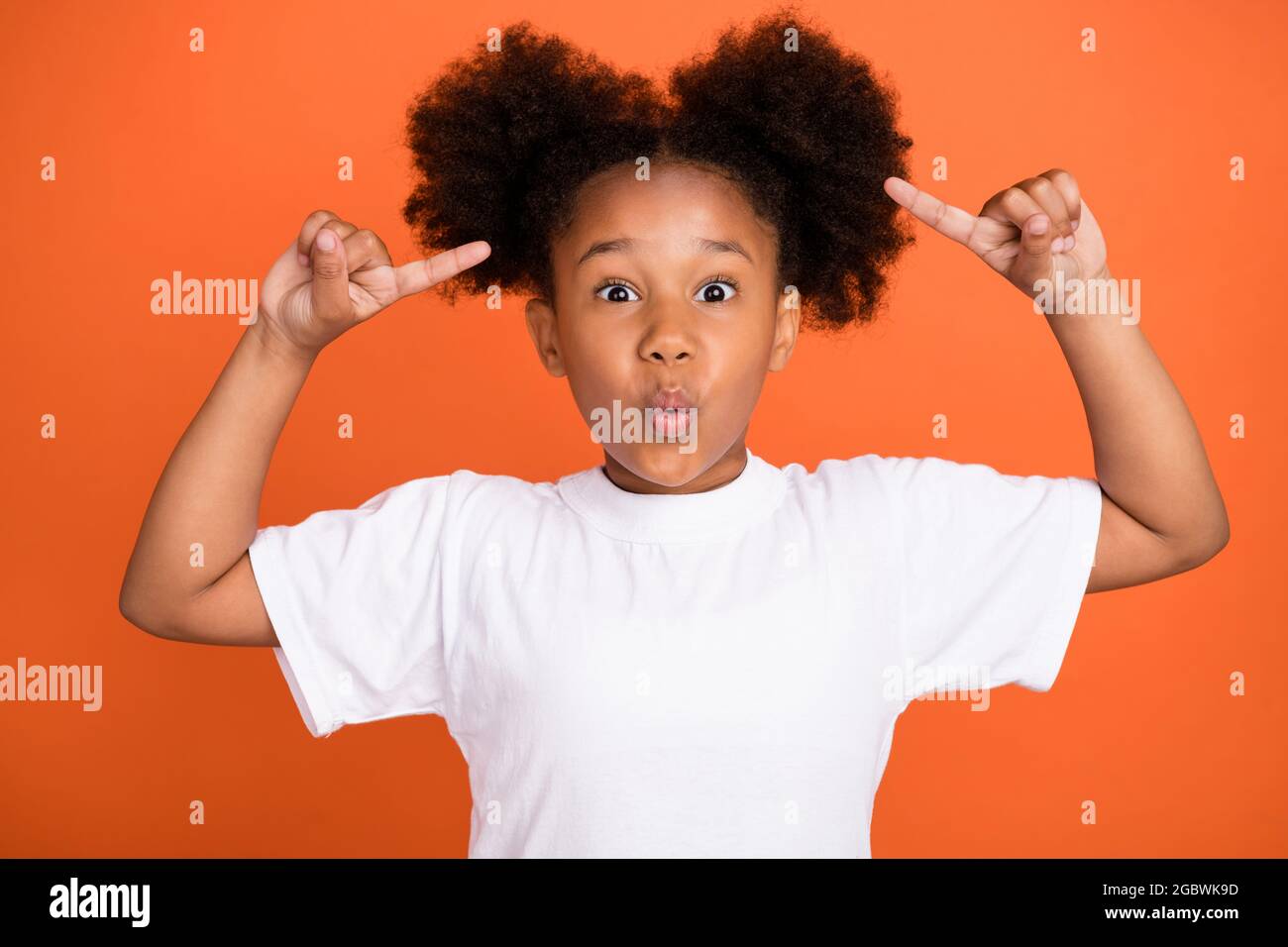 Photo de la petite fille impressionnée pointe cheveux porter un t-shirt blanc isolé sur fond de couleur orange Banque D'Images