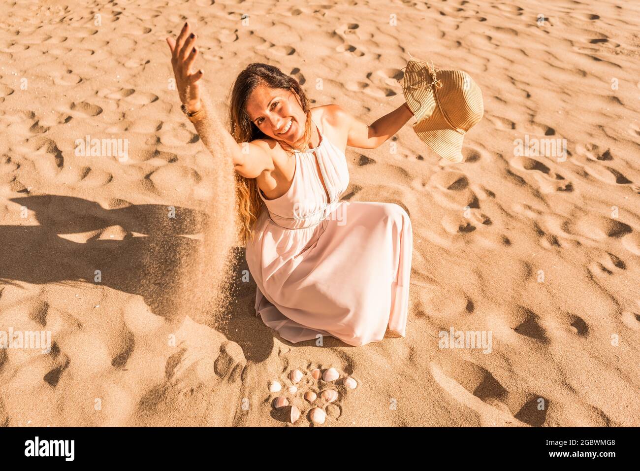 Belle femme caucasienne en robe blanche assise sur la plage jouant avec sable.Summer vacances concept. Banque D'Images