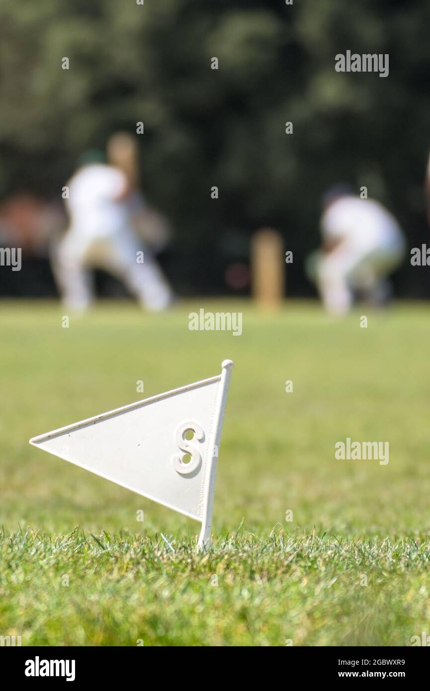 Cricket Boundary Flag Marker avec des hommes jouant du cricket en arrière-plan dans Soft Focus, Angleterre, Royaume-Uni Banque D'Images