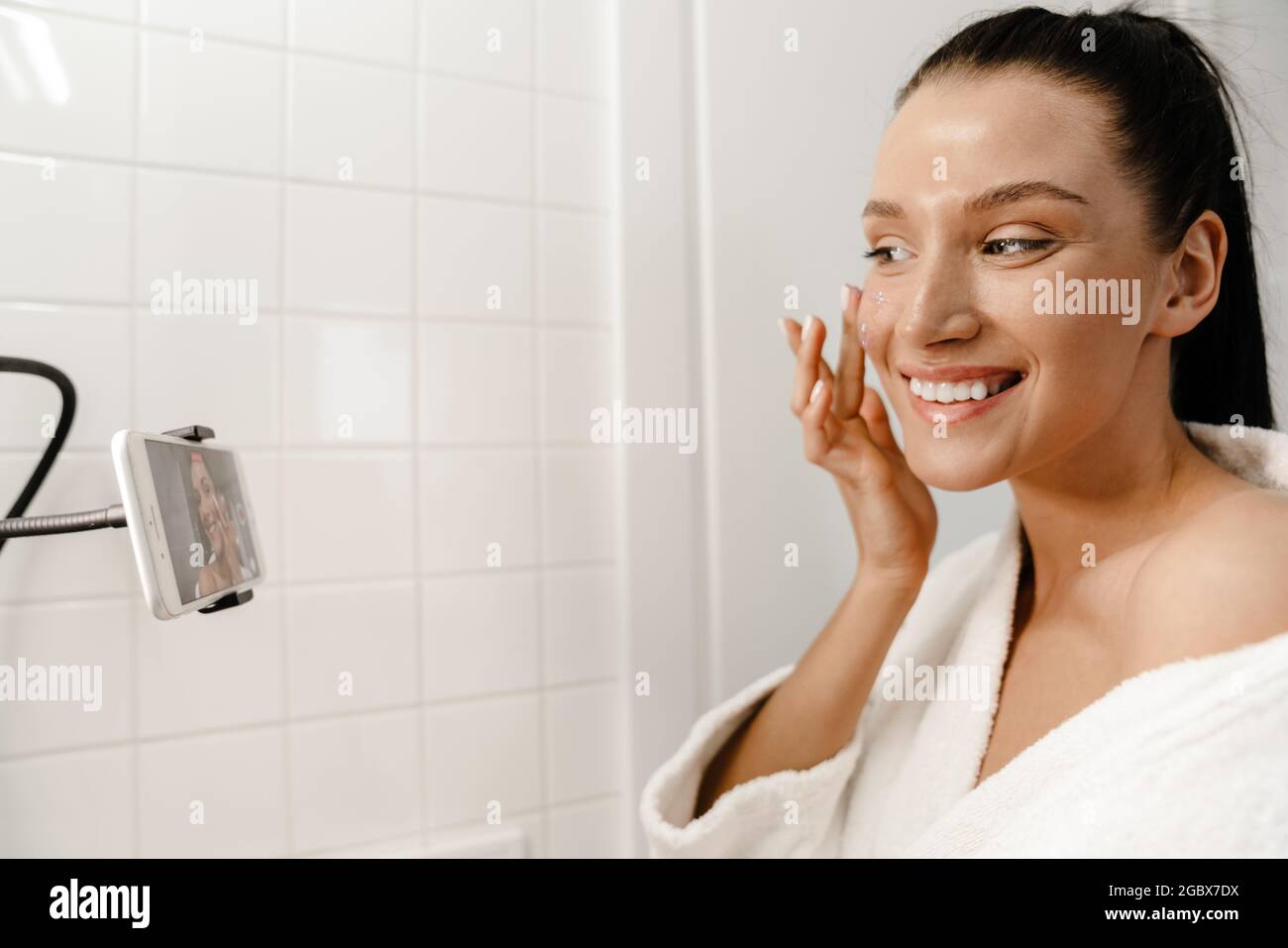 Jeune souriante jeune femme blanche beauté blogger dans bahtrobe faire une  vidéo sur téléphone mobile dans la salle de bains appliquer le gommage du  visage Photo Stock - Alamy