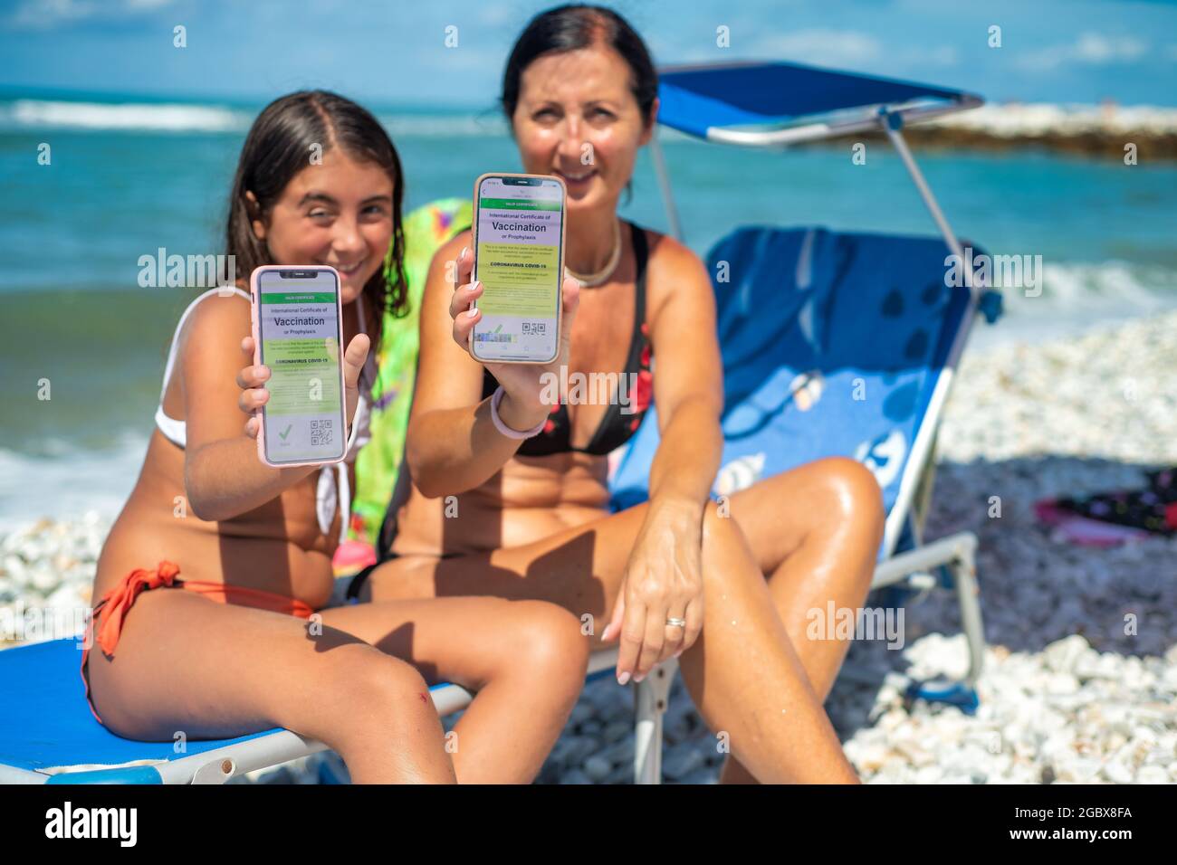 Bonne famille sur la plage avec un pass vert Covid. Femme et fille de 10 ans prêts à partir en voyage avec des captures d'écran de la vaccination Banque D'Images