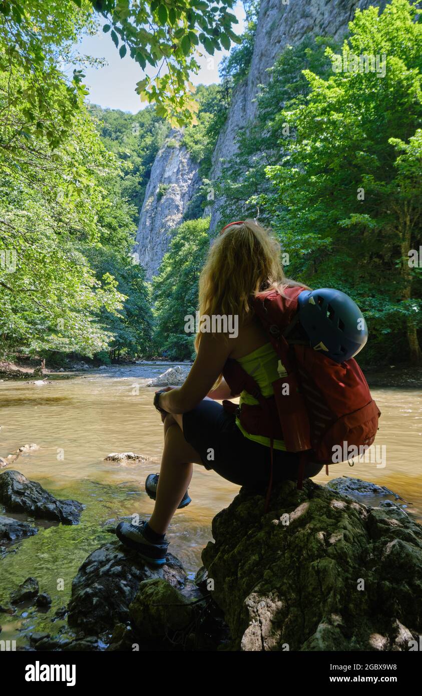 Fille avec un casque d'escalade et un sac à dos se trouve sur un rocher à la gorge de Varghis, montagnes Persani, Roumanie, près de la rivière et des murs verticaux de roche. Été a Banque D'Images