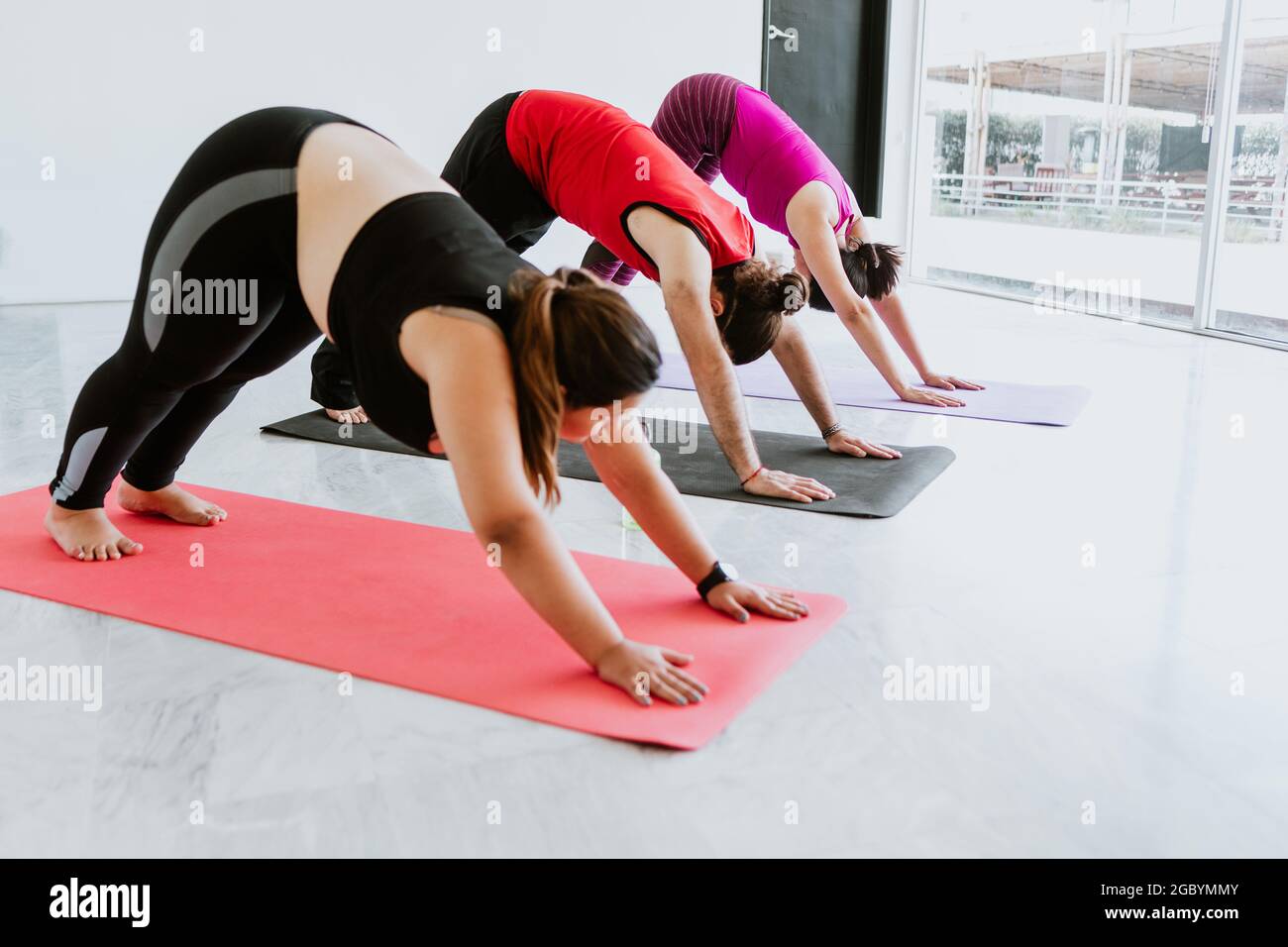 Groupe de personnes latines faisant face à la descente posture de chien dans le studio de yoga en Amérique latine Banque D'Images