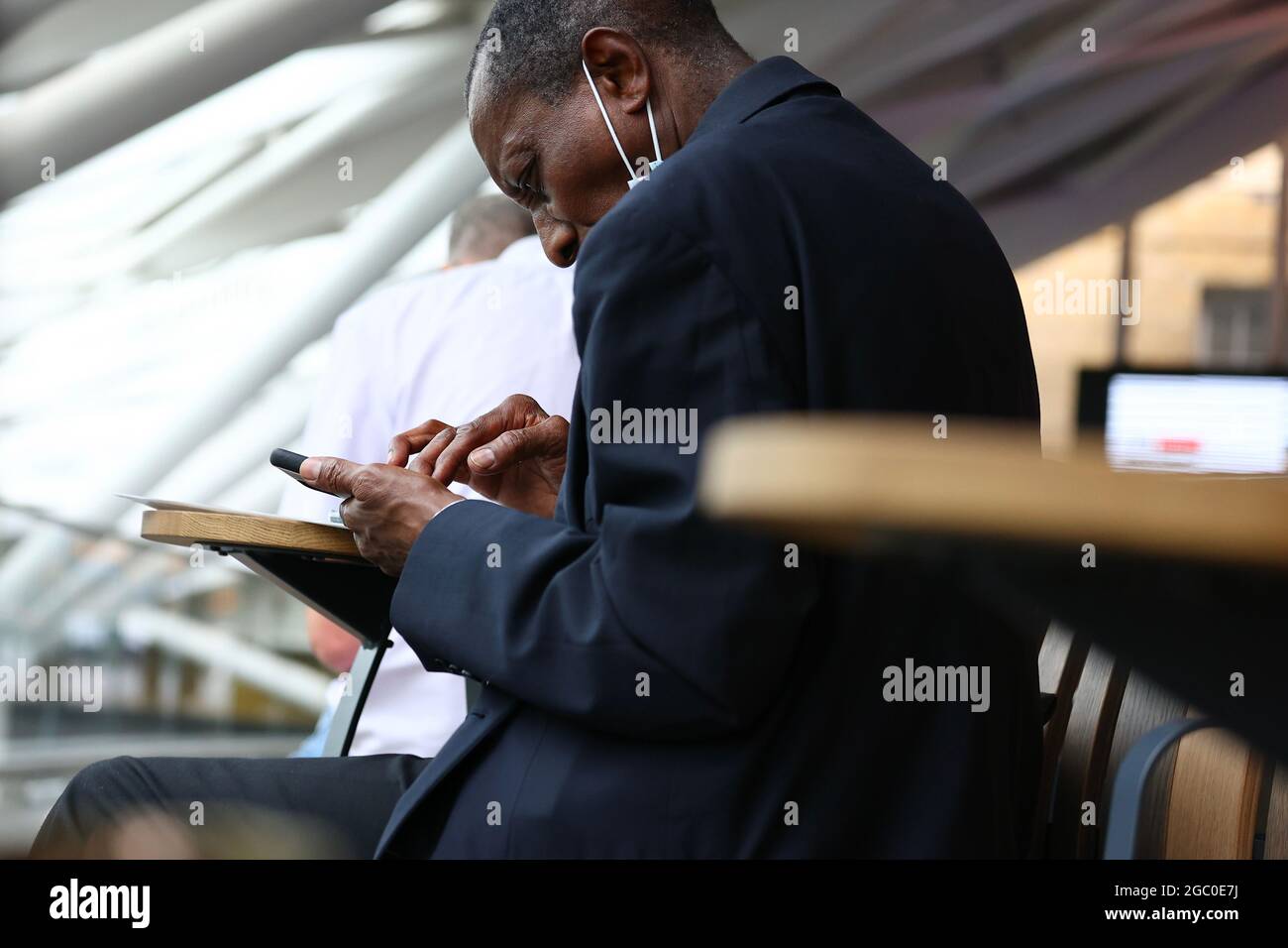 Un homme noir travaillant sur son smartphone à une gare de Londres Banque D'Images