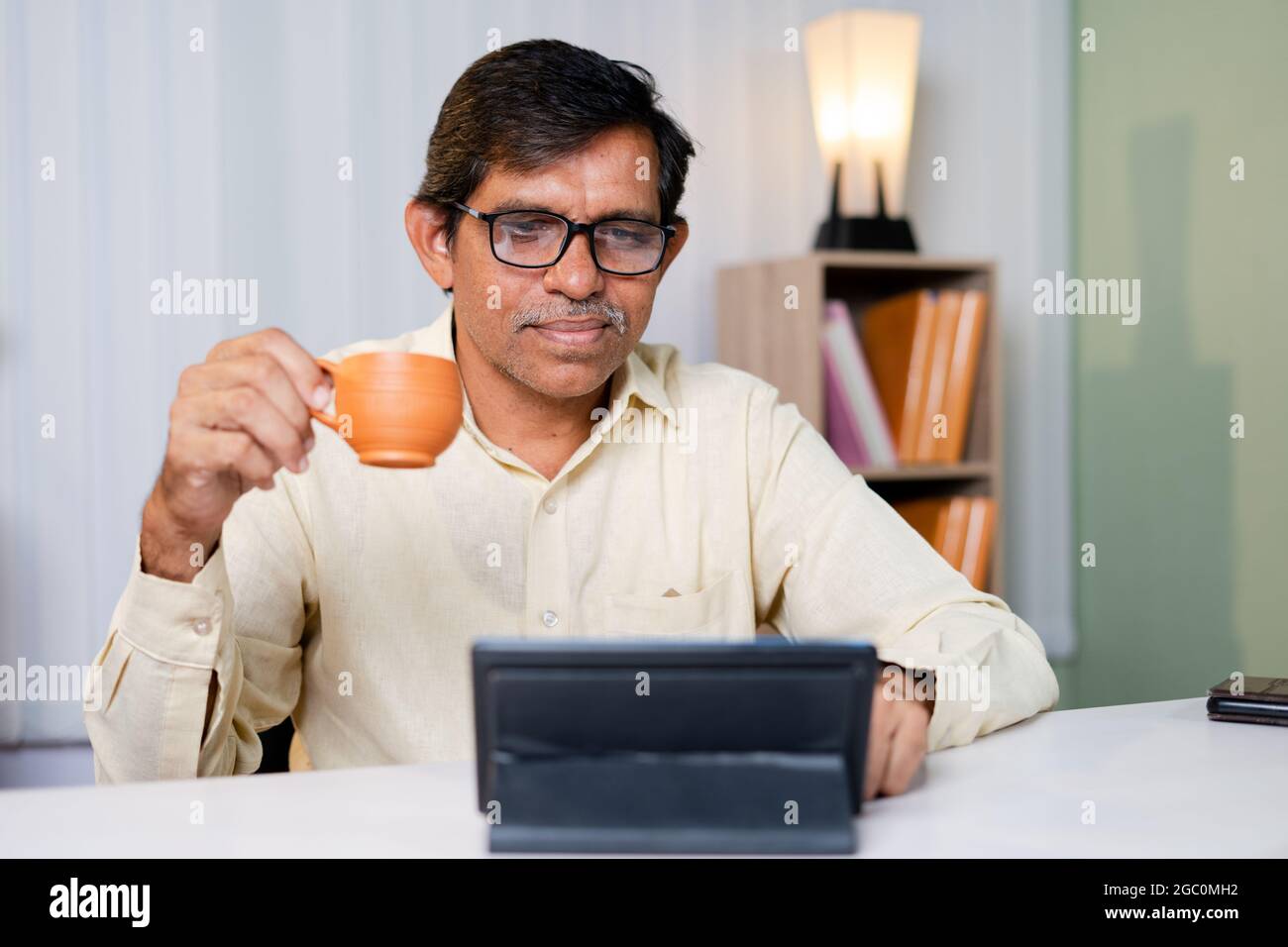 Homme d'affaires prenant un café tout en utilisant ou en lisant des informations, des médias sociaux et Internet sur une tablette numérique au bureau - concept de faire une pause pendant le travail pour Banque D'Images