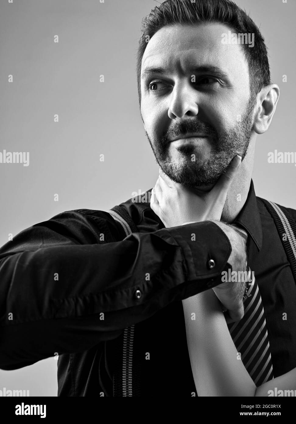 Portrait d'un homme barbu brutal en chemise noire avec cravate rayée et bretelles tenues par une femme près de la gorge Banque D'Images