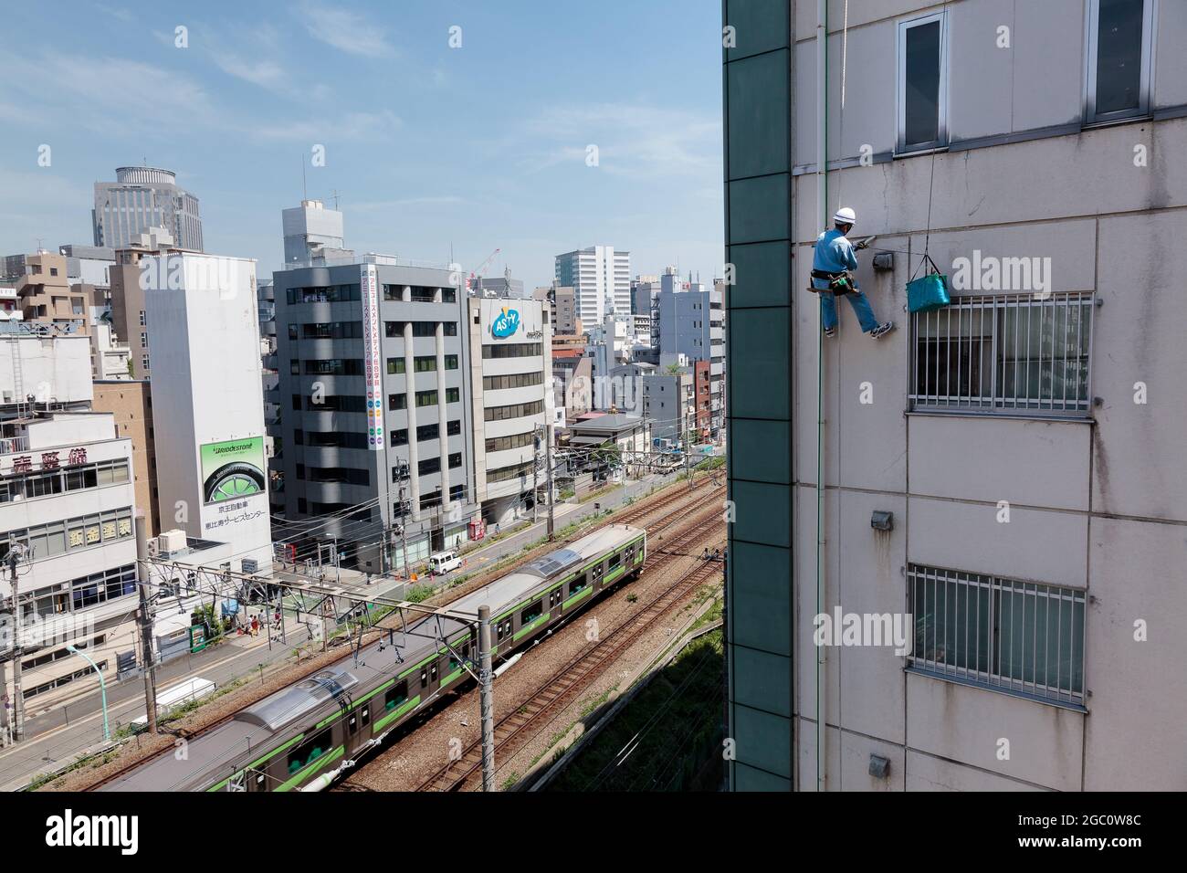 Un technicien d'accès à la corde répare un immeuble d'appartements en passant par un train Yamanote Line. Ebisu, Tokyo, Japon. Banque D'Images