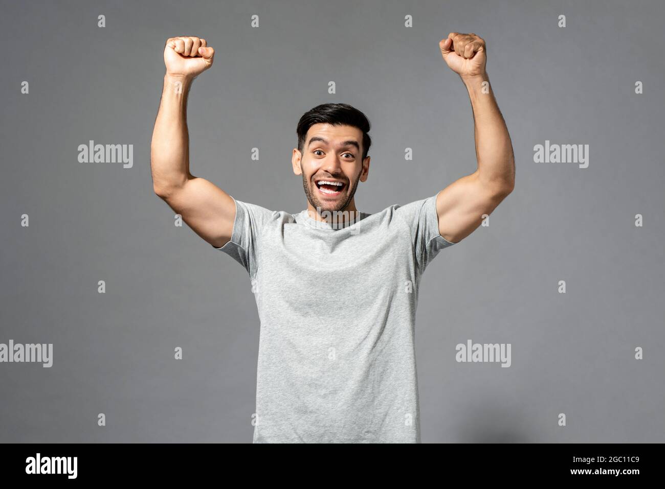 Jeune heureux en bonne santé homme caucasien souriant et élevant ses poings sur fond isolé gris clair studio Banque D'Images