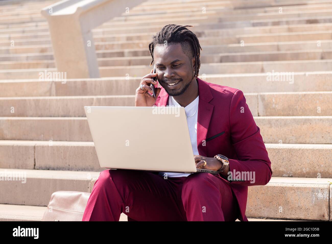 souriant homme noir travaille avec ordinateur portable et téléphone assis sur les escaliers de la ville, la technologie et le concept de travail à distance Banque D'Images