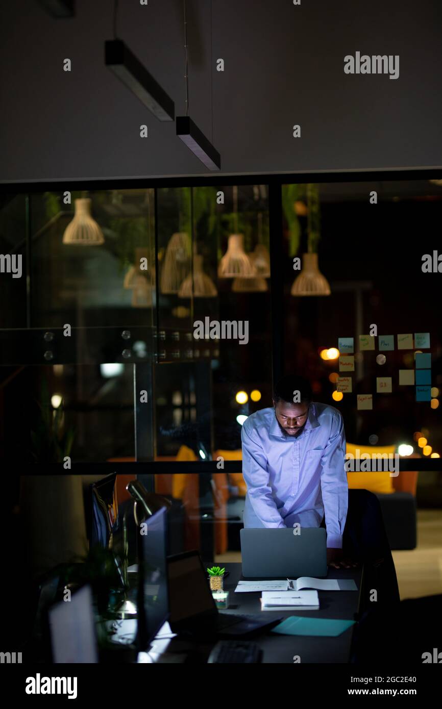 Homme d'affaires afro-américain travaillant la nuit, debout au bureau et utilisant un ordinateur portable Banque D'Images