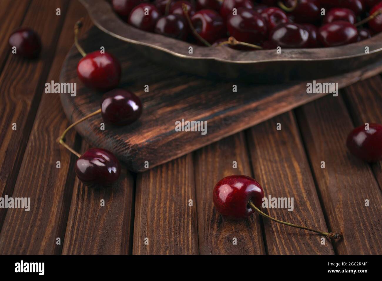 Fruits frais de cerise rouge biologique dans une plaque d'argent vintage sur une ancienne planche à découper texturée en bois sur une table de planches en bois Banque D'Images