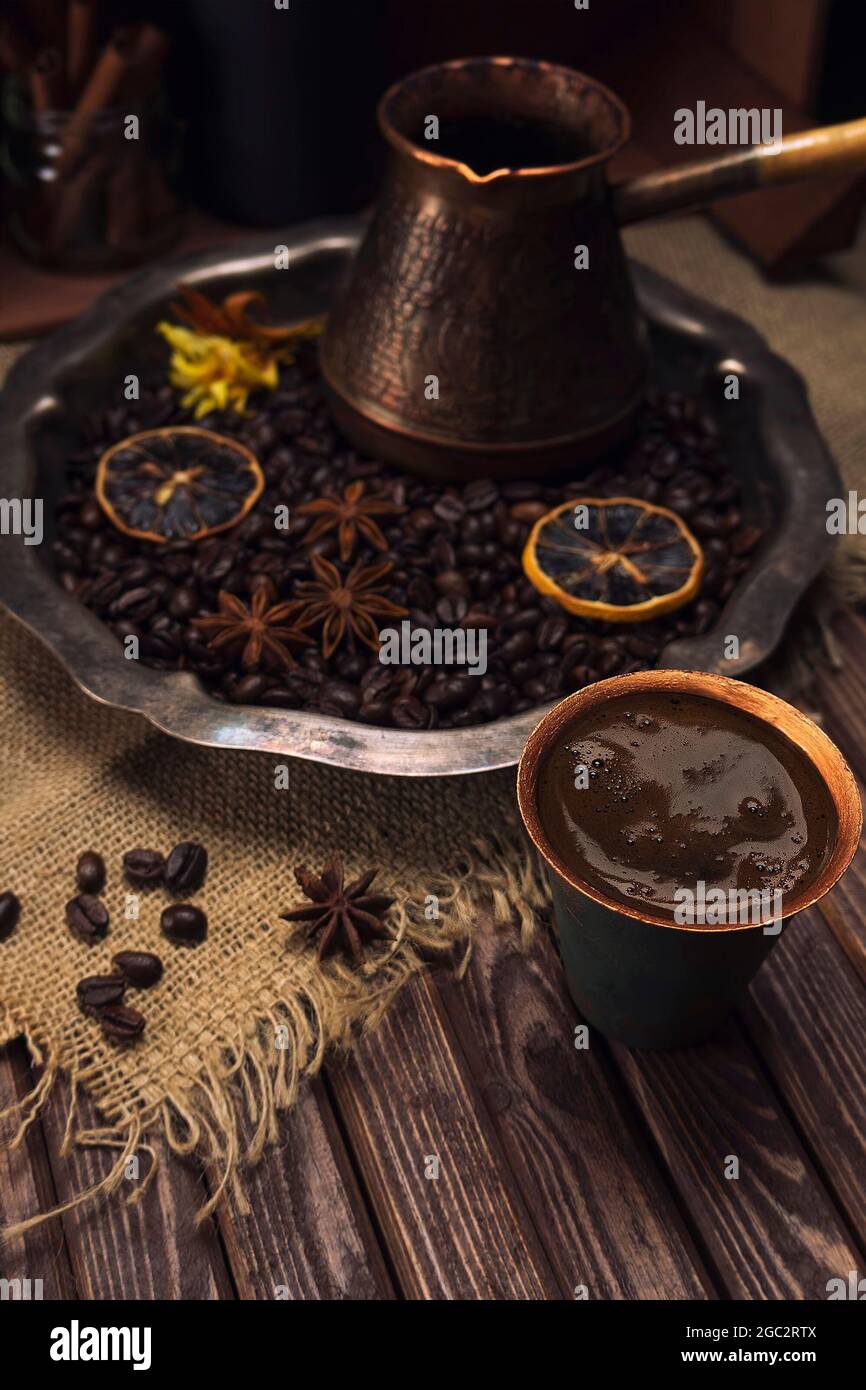 Une tasse de café sur le fond d'un plateau d'argent vintage avec des grains de café, des épices et des fleurs sur une table faite de vieux panneaux texturés en bois Banque D'Images