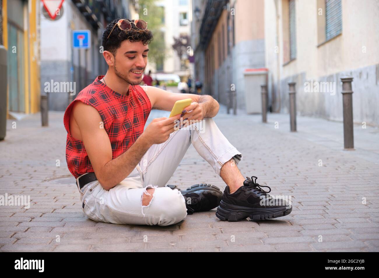 Jeune homme caucasien avec de longs ongles faux en utilisant le téléphone assis sur le sol. Banque D'Images