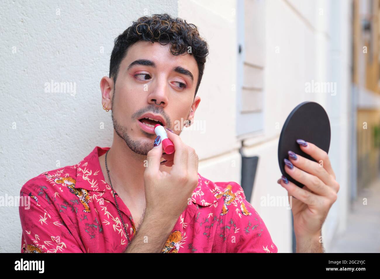 Jeune homme caucasien avec de longs ongles faux appliquant rouge à lèvres dans la rue. Banque D'Images