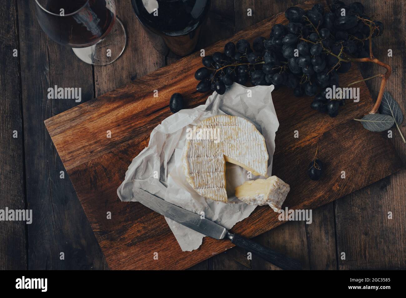 Vue de dessus d'un morceau de fromage et de raisins sur la table en bois et d'un verre de vin en arrière-plan Banque D'Images