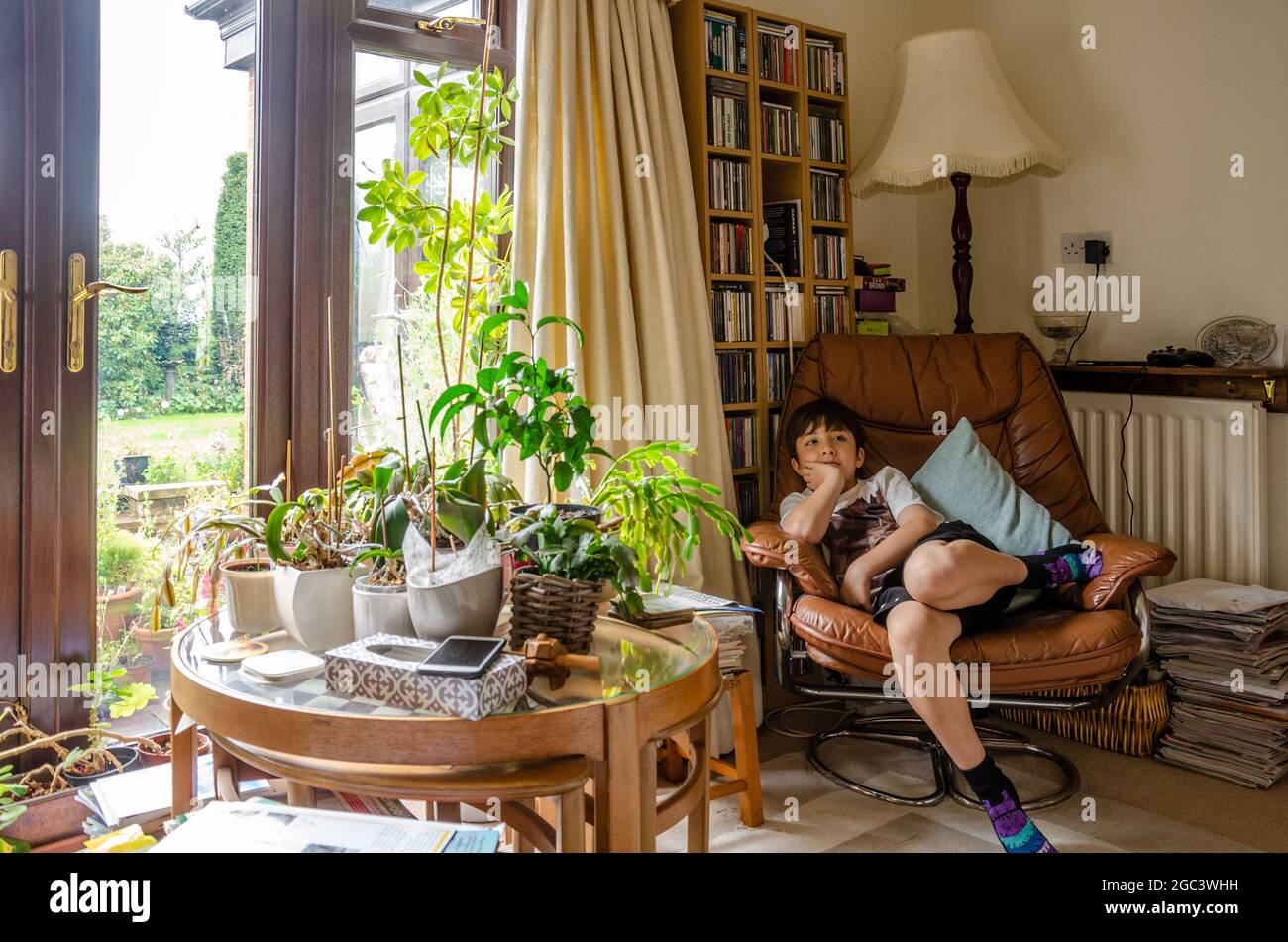 Un garçon se détend dans une chaise confortable avec une table en verre couverte de plantes à l'avant. Une ambiance familiale. Banque D'Images