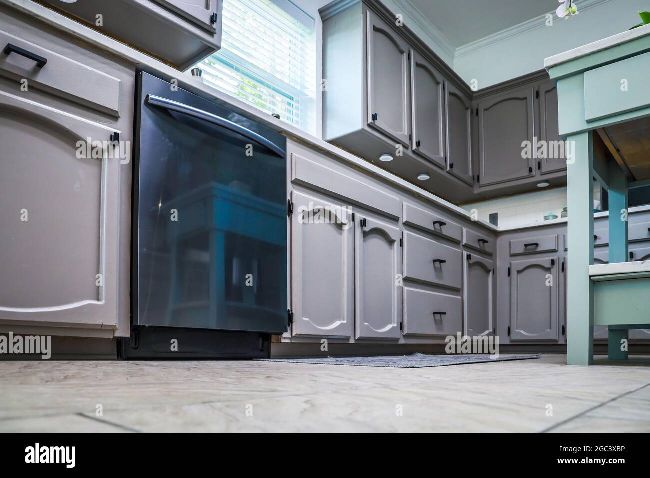 Vue à angle bas d'une cuisine rénovée dans une maison ancienne avec des armoires grises peintes, des comptoirs en marbre, une petite île portable et un sol carrelé Banque D'Images