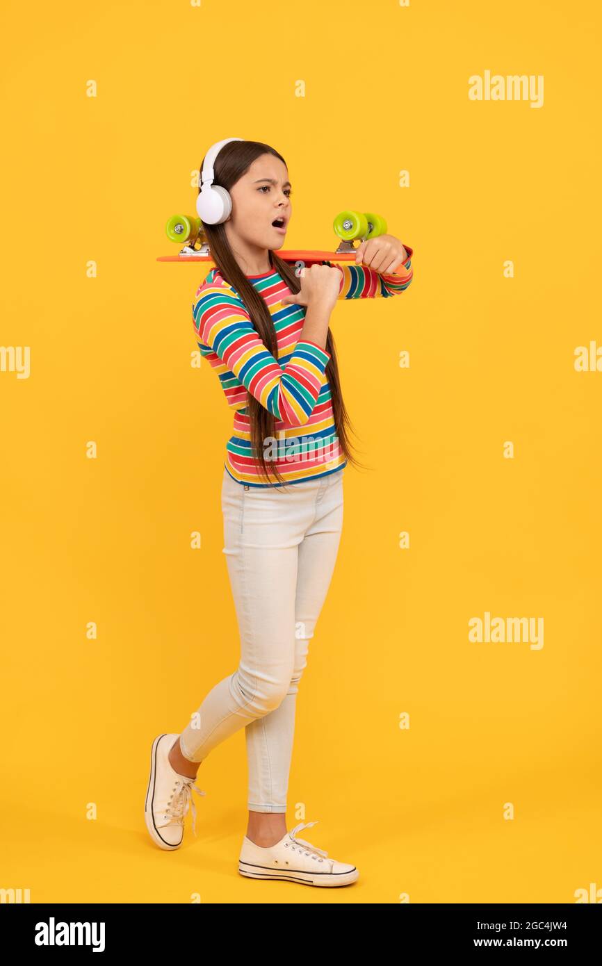 enfant sérieux dans un casque avec un panneau de penny. jeune fille écouter de la musique. activité d'enfance. Banque D'Images