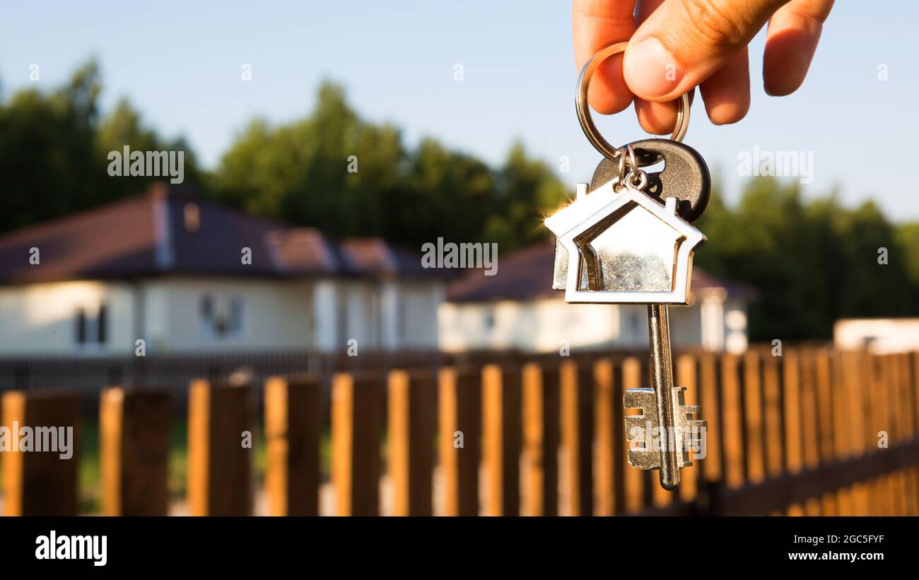 Porte-clés avec porte-clés en main. Arrière-plan de la clôture et du chalet.  Déménagement à une nouvelle maison, hypothèque, achat immobilier, location  et réservation de logements Photo Stock - Alamy