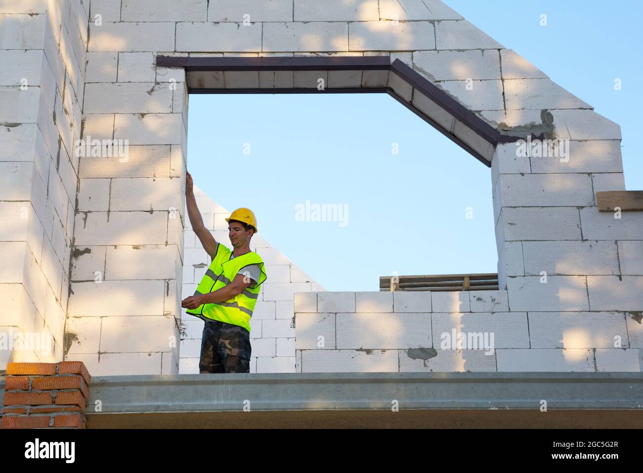 Le travailleur de la construction sur le chantier mesure la longueur de  l'ouverture de la fenêtre et du mur à l'aide d'un mètre ruban. Les chalets  sont en béton poreux Photo Stock -