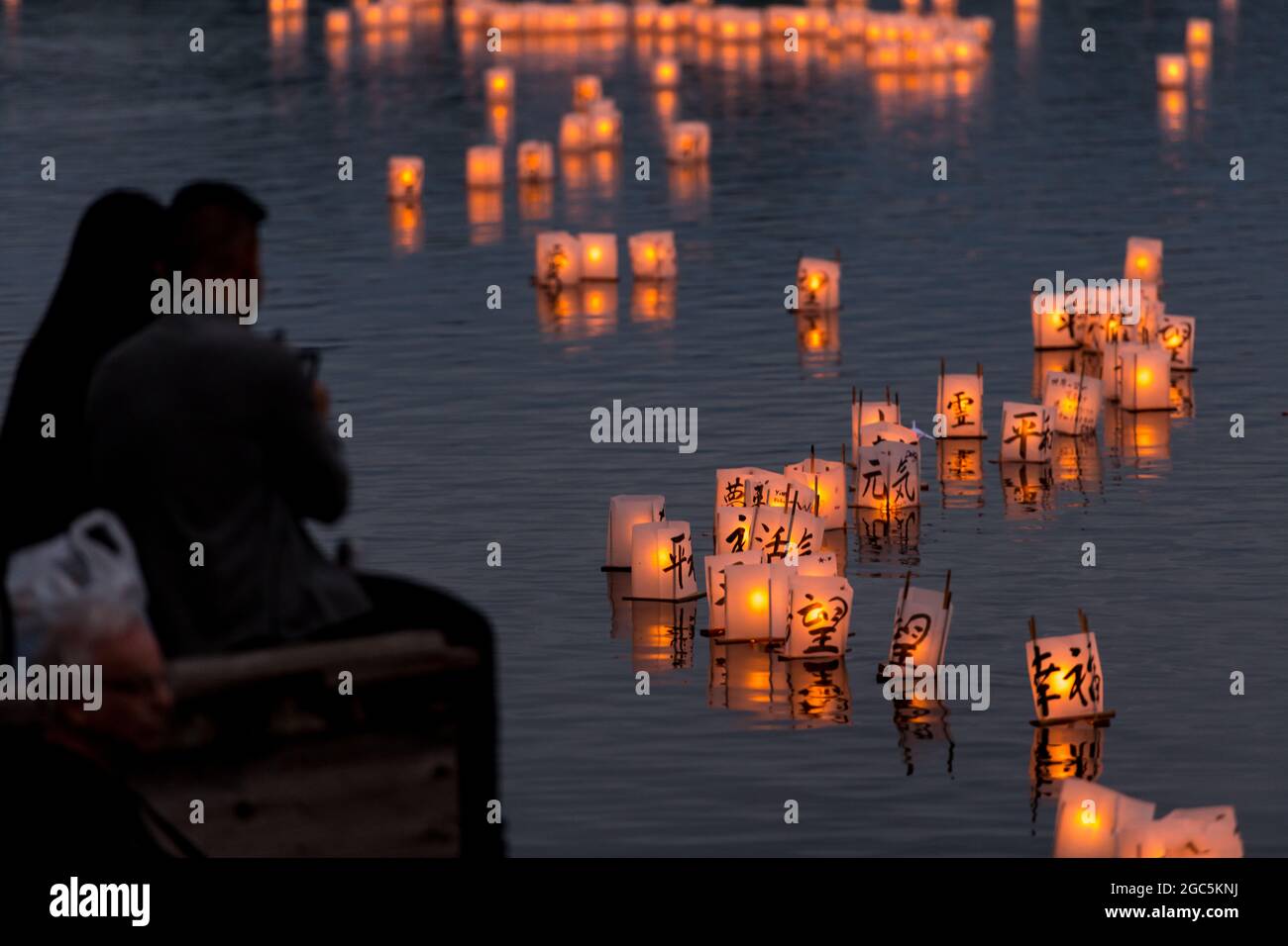 Seattle, États-Unis. 6 août 2021. Au crépuscule, les gens regardent les lanternes flottantes en papier de riz au mémorial du 76e anniversaire de Hiroshima à Hope. Les gens se rassemblent chaque année sur les rives du lac Green, juste au nord du centre-ville de Seattle, ils éclairent les lanternes en papier de riz avec des bougies dans les mémoires des victimes de l'attentat à la bombe nucléaire d'Hiroshima pendant la deuxième Guerre mondiale. Crédit : James Anderson/Alay Banque D'Images