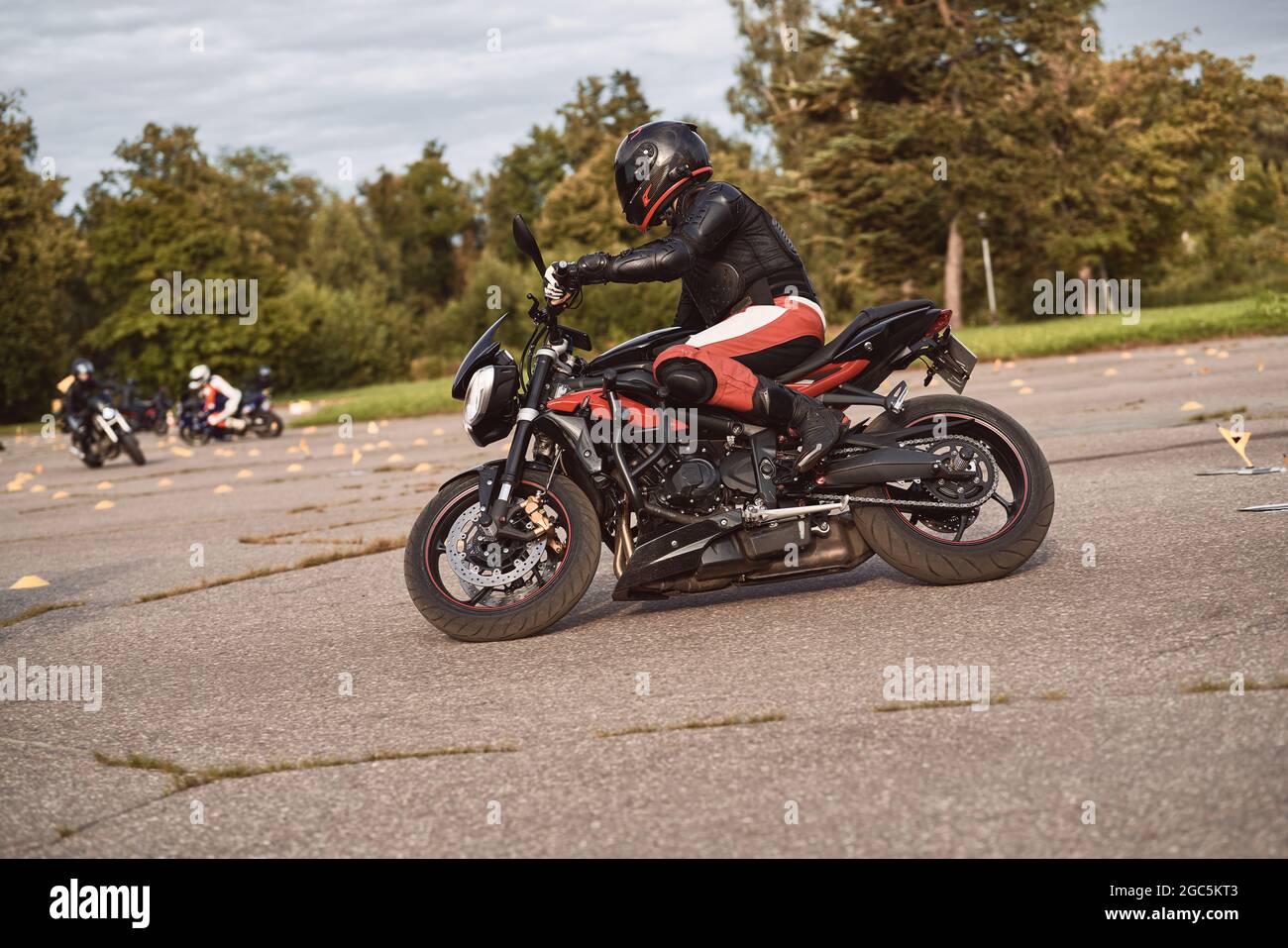 Un motard masculin portant un costume de course en cuir de protection avec  une moto ou une moto rouge sur une route à ciel ouvert. L'image est prise  en mode HDR et