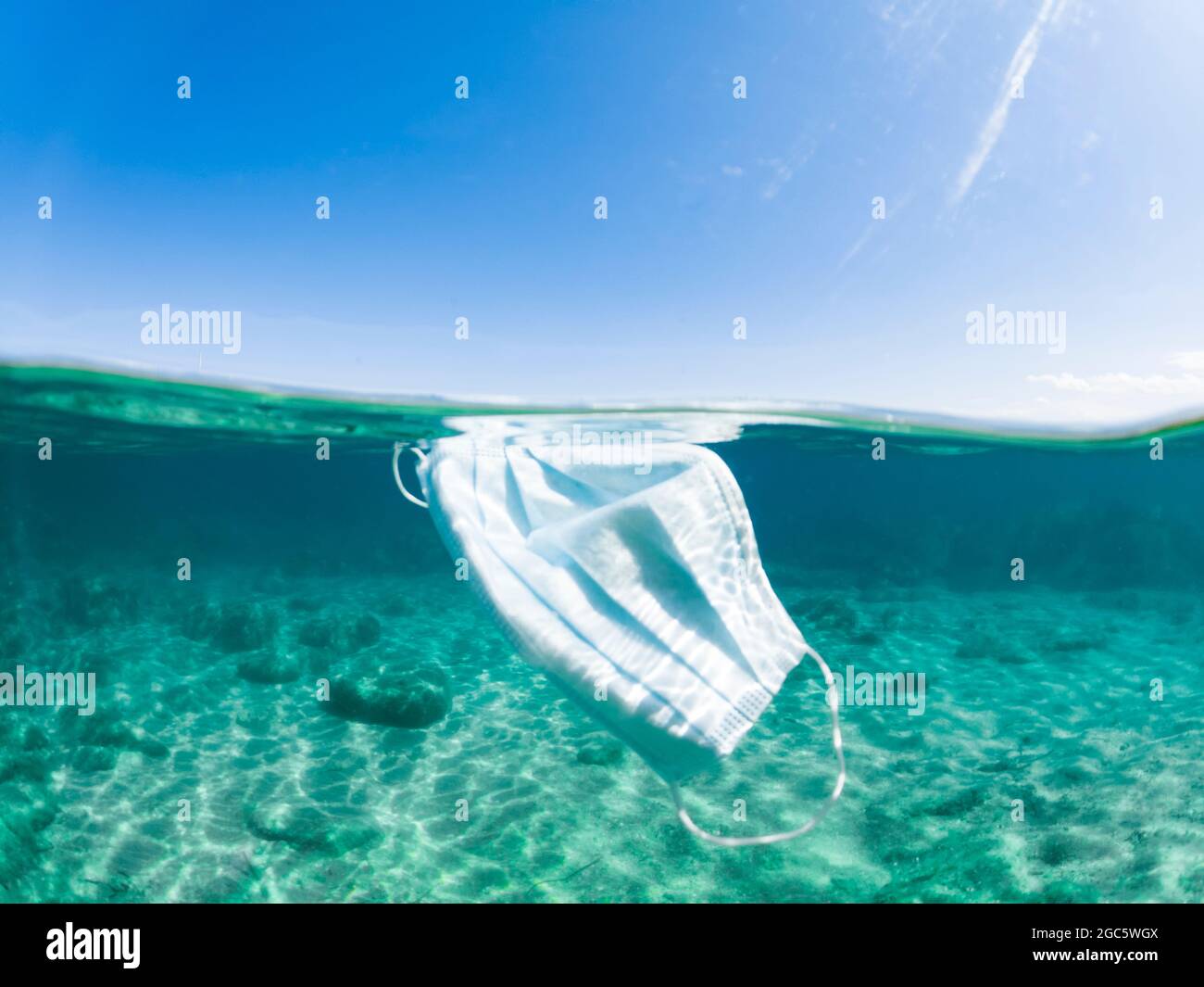 Un masque chirurgical à jet partagé, défoqué, flottant dans une eau turquoise. Concept de pollution de la mer pendant la pandémie de Covid-19. Sardaigne, Italie. Banque D'Images