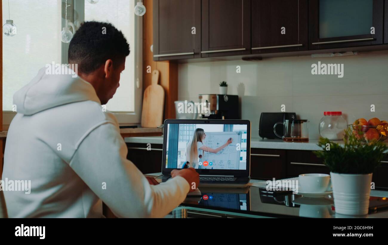 Vue arrière de l'homme africain regardant la vidéo en ligne sur ordinateur et prenant des notes. Il travaille à la maison en quarantaine. Banque D'Images
