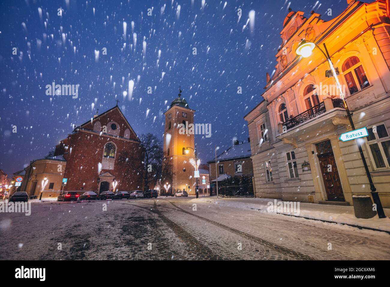 Pologne, Subcarpathia, Rzeszow, rue illuminée avec église en hiver chute de neige la nuit Banque D'Images