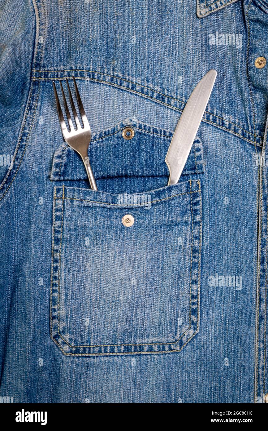 Couteau et fourchette dans la poche brest d'une veste en denim. Banque D'Images