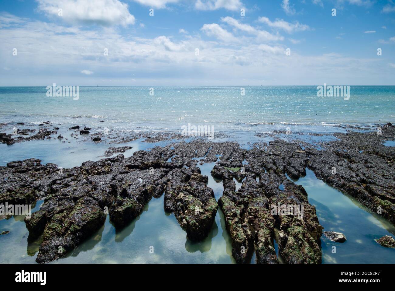L'horizon d'une mer calme avec les rochers exposés à marée basse avec un ciel bleu et des nuages cumulus le jour ensoleillé de l'été. Banque D'Images
