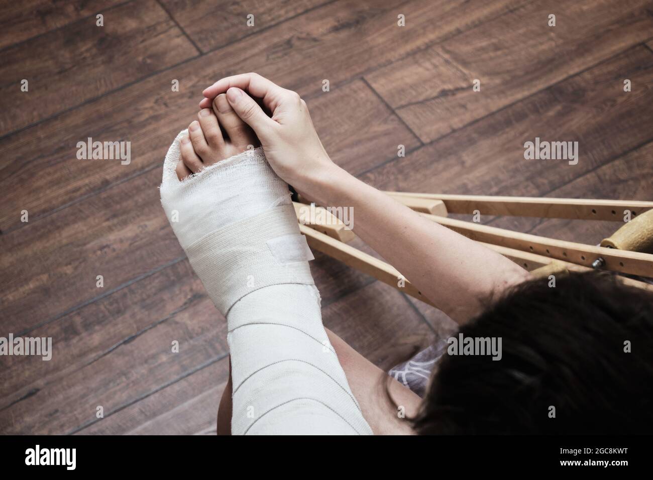 Une femme masse les orteils d'une jambe cassée avec ses mains. Vue de dessus d'une jambe cassée dans un plâtre et des béquilles. Réhabilitation à domicile après une rupture Banque D'Images