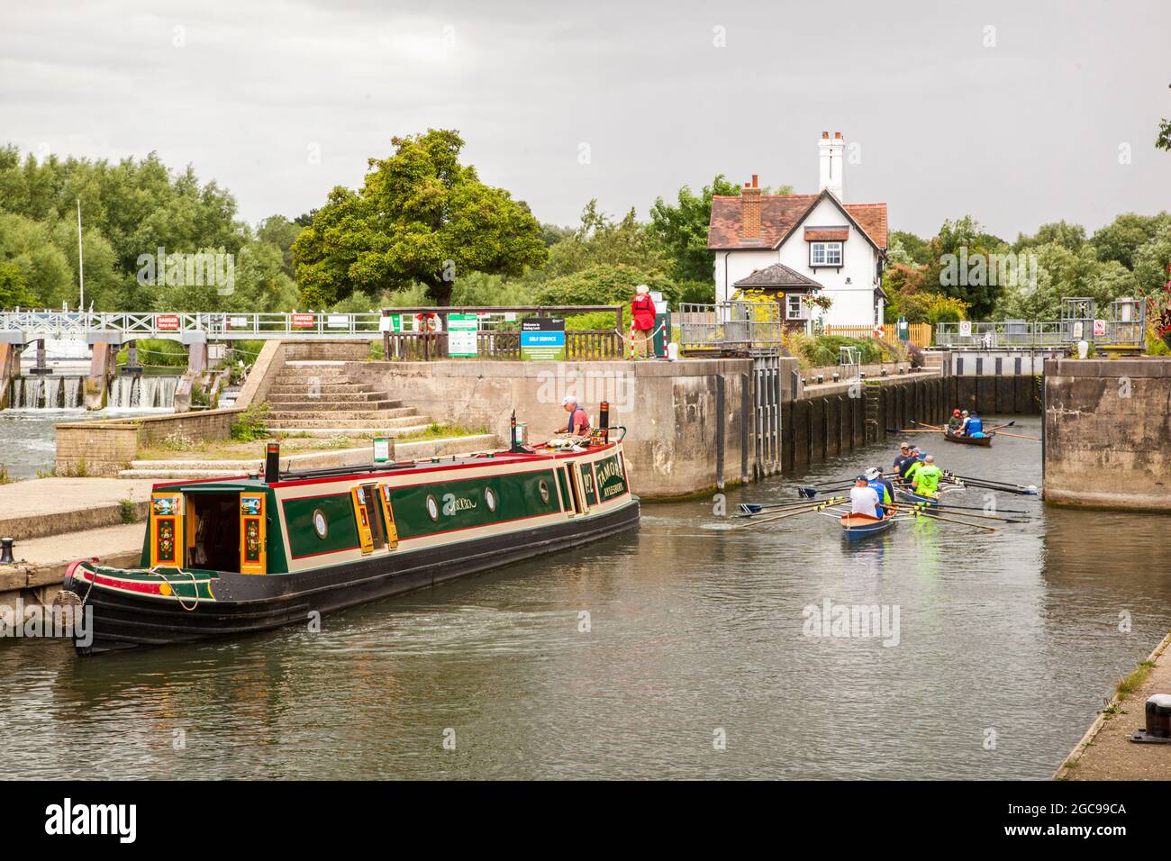 Bateau étroit sur le canal et personnes dans des bateaux à rames passant par les écluses sur la Tamise à Goring Oxfordshire Angleterre Banque D'Images