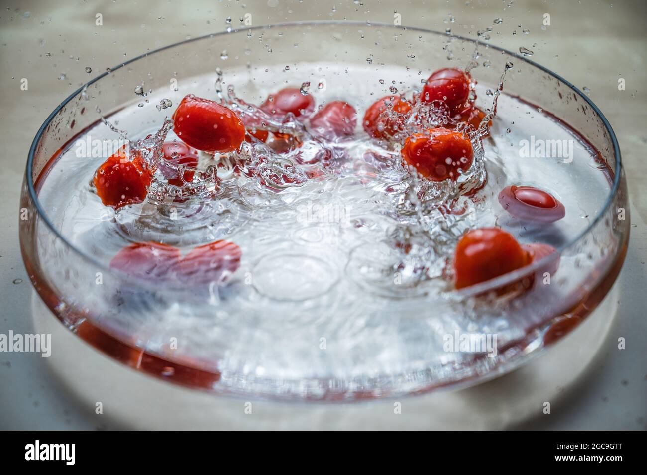 Gros plan des tomates cerises et prune de bébé de légumes biologiques rouges frais (tomate bébé, tomate cerise) en groupe sur le bol d'eau avec des éclaboussures d'eau Banque D'Images