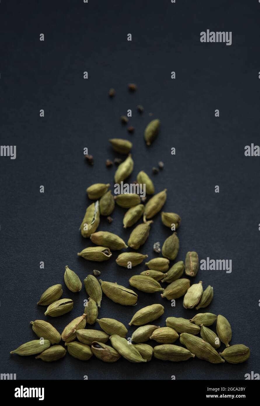 Photo verticale de petits DOF gros plan des gousses de Cardamom et des grains de la pile sur le fond noir mat. Il est très populaire dans la cuisine indienne et Sri Lanka. Banque D'Images