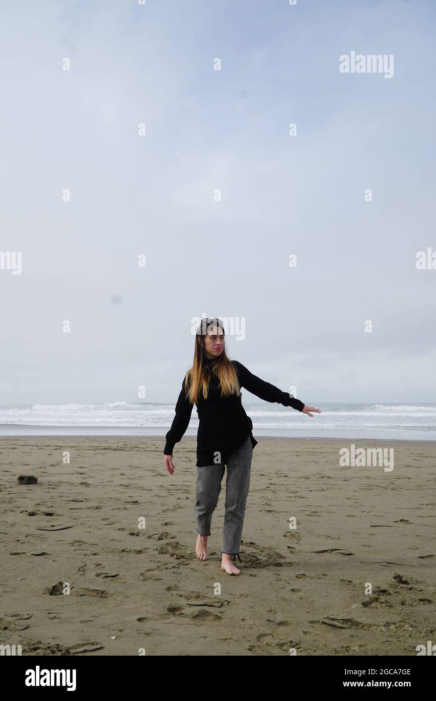 Fille sur la plage de sable. Une fille dans une veste noire sur la mer.  Migrants en Amérique. Une jeune femme marche rêveur sur le sable. La mer  dans le ciel nuageux