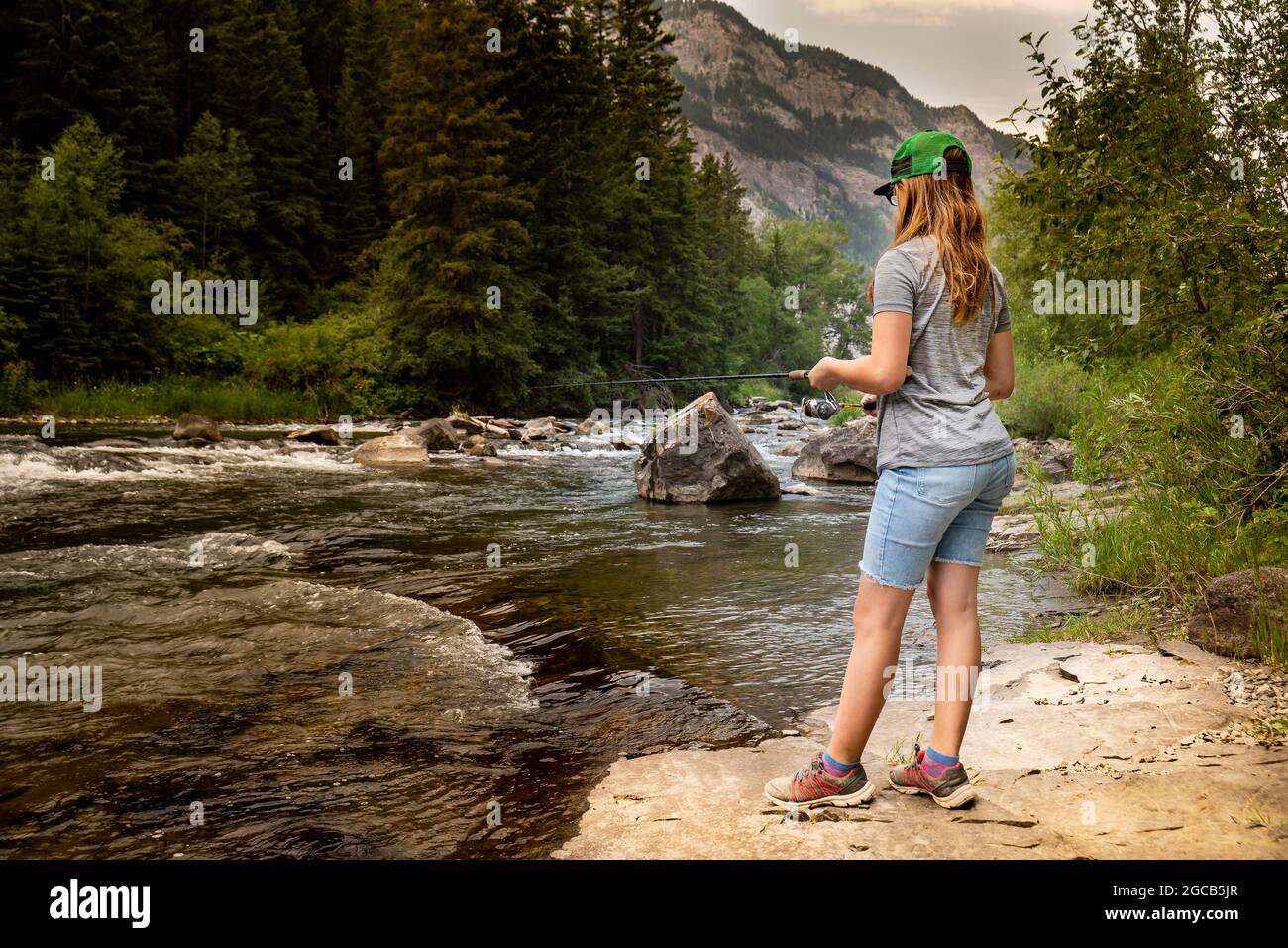 Une jeune fille pêchant un ruisseau de montagne à partir d'un rocher en Alberta au Canada. Banque D'Images