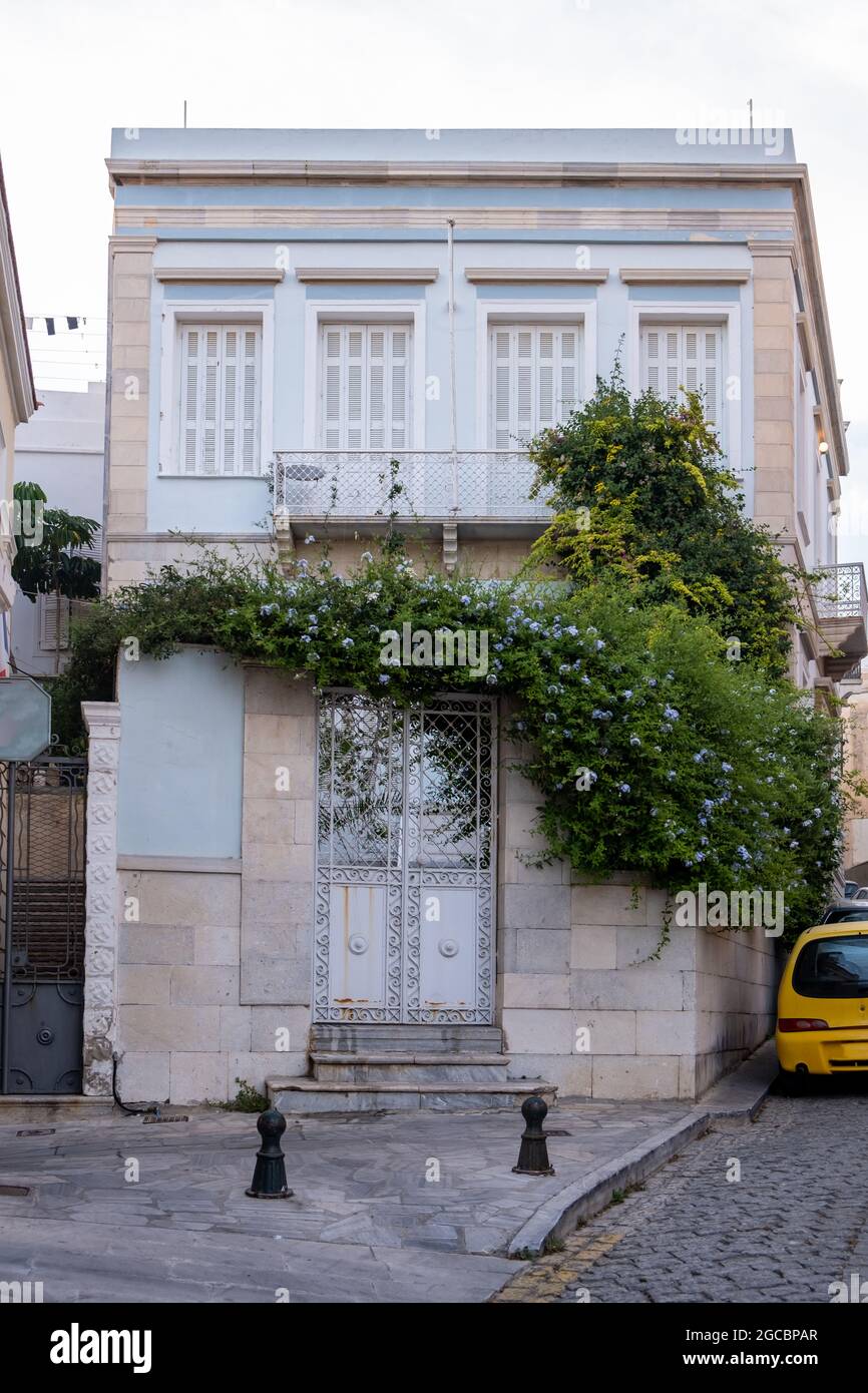 Maison traditionnelle murale en marbre avec volets fermés porte métallique pavée. Une plante verte Morning Glory entoure un bâtiment avec balcon à Syros i Banque D'Images