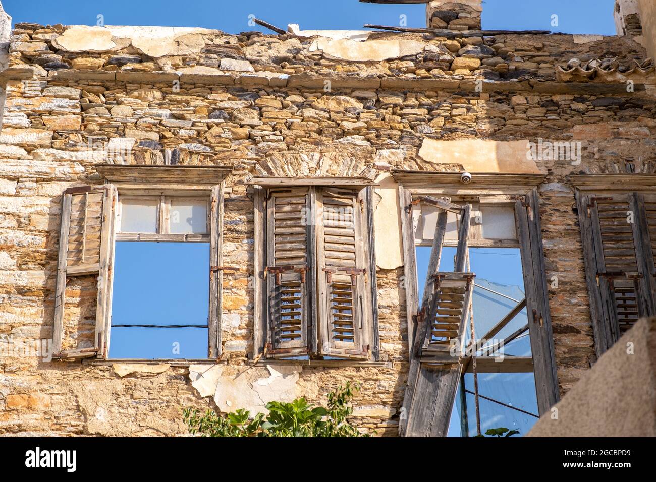 Bâtiment en pierre endommagé, volets en bois vieux cassé et fenêtres avec vue sur le ciel bleu. L'abandon de la vieille maison de décomposition ruiné la structure négligée à Syros Banque D'Images