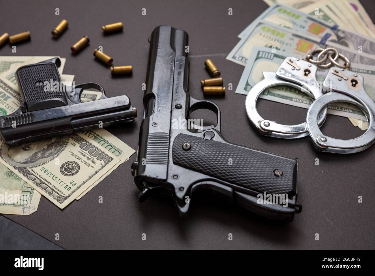 L'argent criminel et la peine. Pistolets et obus de balle 9 mm, menottes et billets en dollars américains sur fond noir. Crime et droit, Banque D'Images