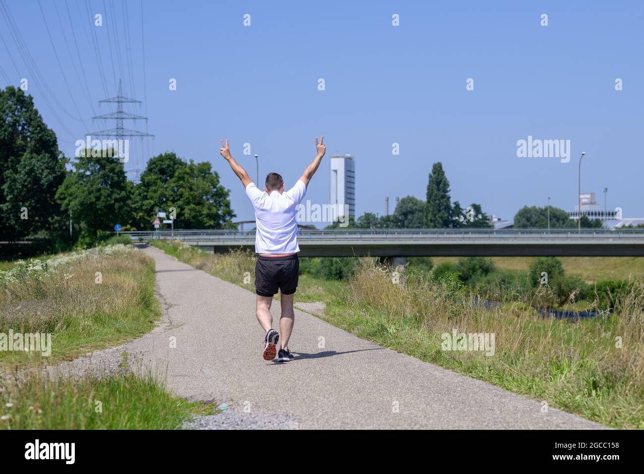 Un homme senior s'éloigne de la caméra en faisant un panneau en V le long d'un sentier le long d'un canal lors d'une journée d'été ensoleillée dans le concept d'une outd active saine Banque D'Images